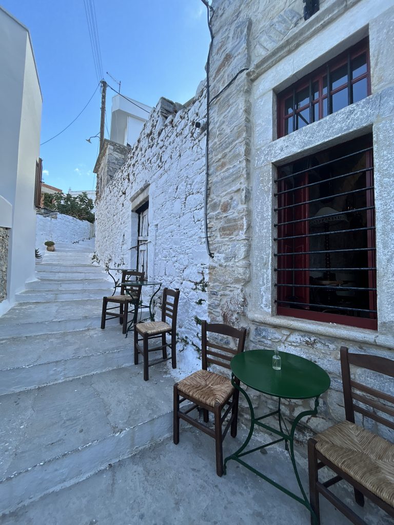 Walking through a narrow, whitewashed alleyway in a traditional Naxos mountain village, featuring stone-paved streets, blooming bougainvillea, and classic Cycladic architecture.